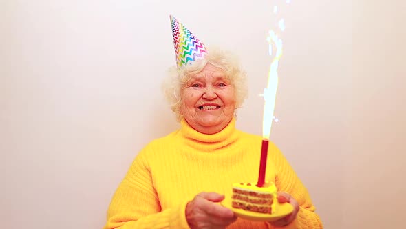 Older Woman with a Gift Wear Yellow Sweater and Horn Cap on a White Background Holding Plate with