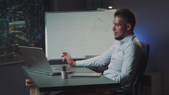 Young Latino Man Providing Video Conference Call on Computer at Office at Night