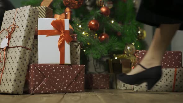 Woman Walks Up To the Christmas Tree and Takes Gift Box From Stack of Gifts Lying on the Wooden