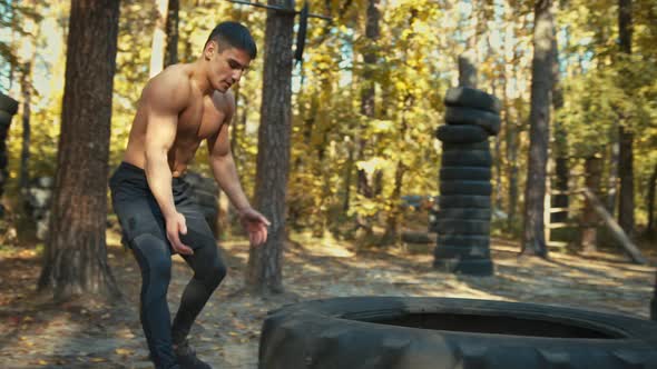 Man working out with a huge tire, turning and flipping in the forest gym. Strength and motivation