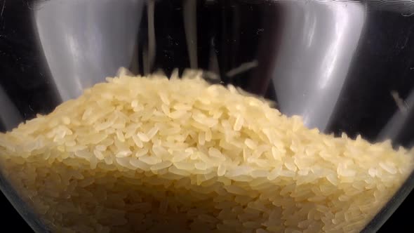 Rice is poured into a glass bowl on a black background.