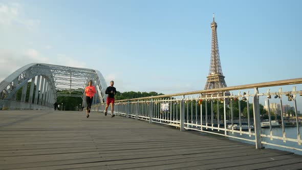 A man woman couple running across a bridge with the Eiffel Tower