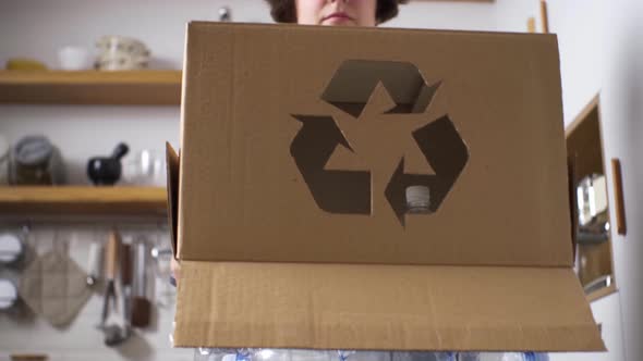 Woman In Kitchen Covers Plastic Bottles With A Cardboard Box With A Recycle Sign. Plastic Recycling