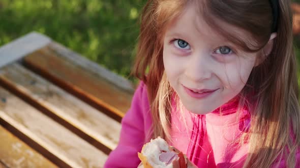 Cute Child in a Pink Jacket Eating a Hot Dog Outdoors