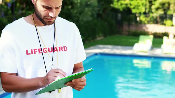 Smiling lifeguard writing on clipboard at poolside