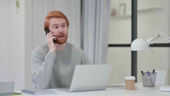 Redhead Man with Laptop Talking on Smartphone 