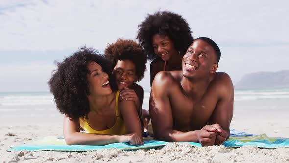 Portrait of african american parents and two children lying on a towel at the beach smiling