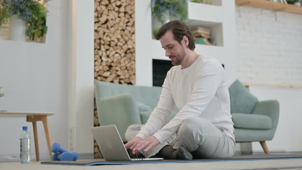 Young Man Using Laptop on Yoga Mat at Home