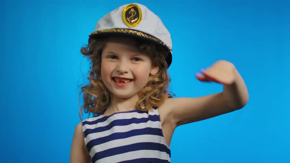 Little Curly Sailor Girl Puts Her Hand to the Cap and Smiles in the Studio