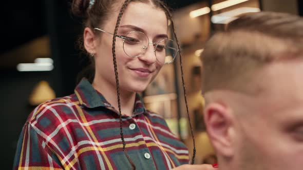 Barbershop: girl hairdresser smiles while cutting a man's hair with a razor