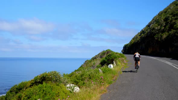 Female cyclist cycling on a coastal road on a sunny day 4k