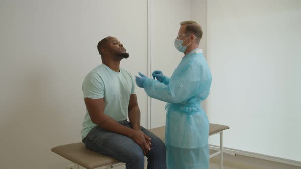 Male Physician in PPE Taking Black Patient Swab Sample for PCR Test for Coronavirus at Hospital