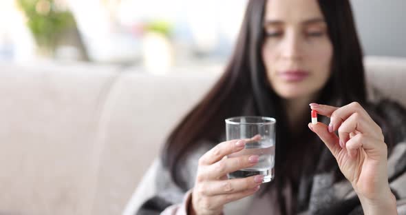 Woman on the Couch Holding a Capsule and a Glass of Water