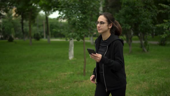 A Young Woman is Jogging with Her Phone in the Park