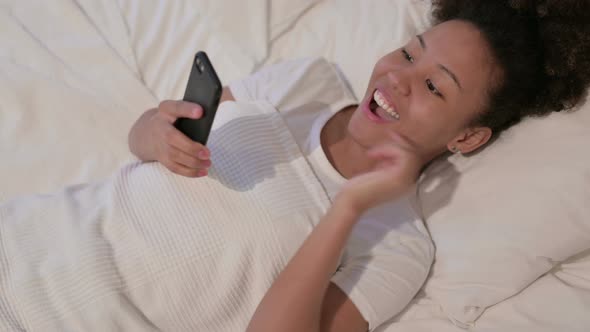 African Woman Celebrating Success on Smartphone in Bed