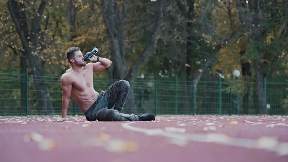 Shirtless sportsman drinks water on the stadium. 
