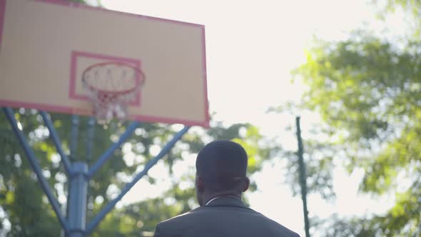 Back View of African American Man in Formal Suit Throwing Ball Into Hoop and Making Victory Gesture