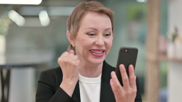 Old Businesswoman Celebrating Success on Smartphone 