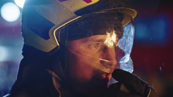 Portrait Shot of a Fireman in Action Speaking on the Walkie Talkie. Fire Reflection on the Helmet