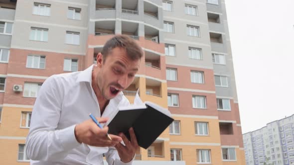 Happy Businessman in a White Shirt Makes a Note in a Notebook