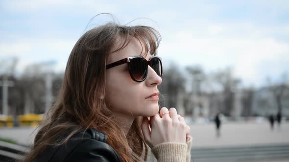 Side View of a Young Sad Girl Portrait in Sunglasses Sits on the Street of Her City and Yearns