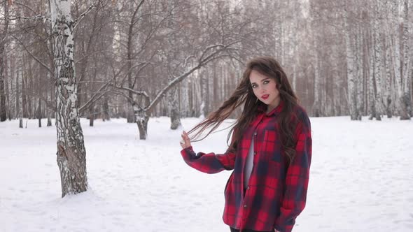 Young Woman with Wavy Hair Standing and Touching Face in Winter Forest