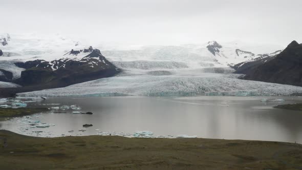 Iceland glacier with water, green grass, blue ice and fog with drone video moving up.