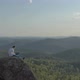 Aerial View of a Young Man Working on a Laptop Sitting on Top of a Rock Mountain in the Forest - VideoHive Item for Sale