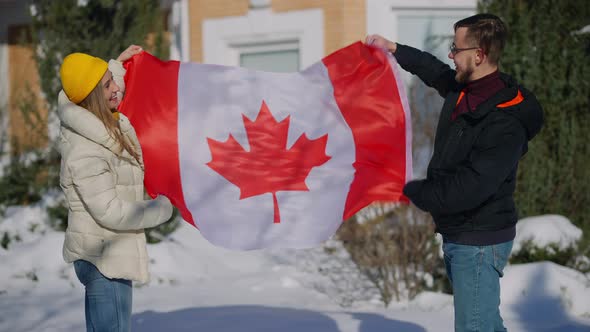 Young Happy Canadians Posing with National Flag Fluttering in Hands Outdoors on Sunny Winter