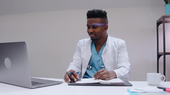 Black Man Talking in Video Chat on Laptop Wearing Medical Gown and Stethoscope