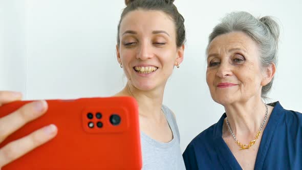 Adult Daughter and Senior Mum are Taking Selfportrait Picture Selfie on Red Smartphone Together