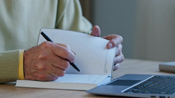 Closeup Hand of Elderly Caucasian Man Write Notes in Personal Paper Planner at Desk Unrecognizable