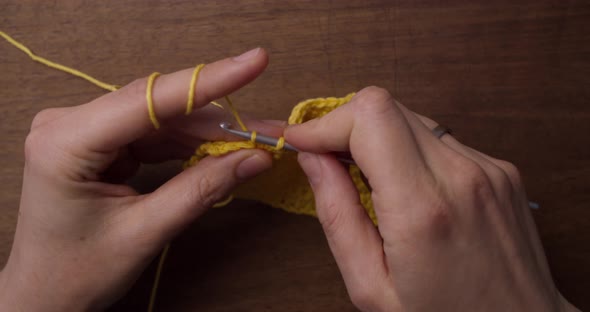 Close up top shot of caucasian hands doing some needle work: crochet. Yellow wool laying on the tabl
