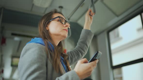 Woman with Glasses in Tram Using Smartphone Chatting and Texting with Friends During the Trip