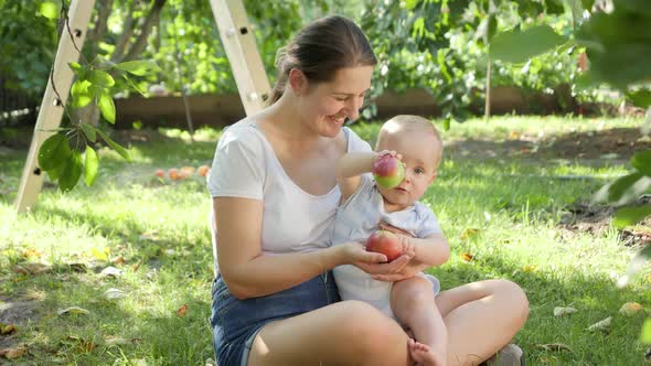 Young Mother Hugging and Smiling at Her Baby Son Holding Ripe Red Apples at House Backyard Garden