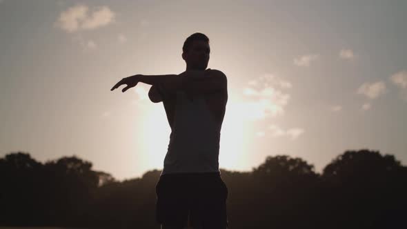 Young Attract Man Stretches In Park Before He Goes For A Run With The Evening Sun In The Background