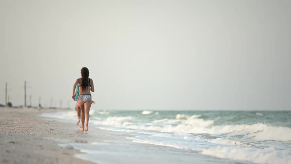 Two Sisters in Swimsuits Run Along the Beach and Enjoy a Summer Evening