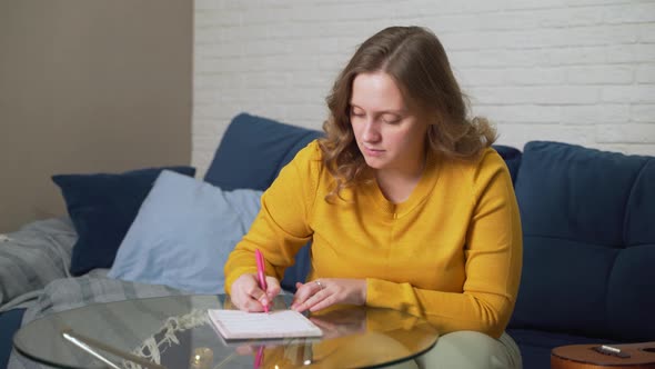 Woman is Writing Something on Sheets of Paper at Glass Table with Pen