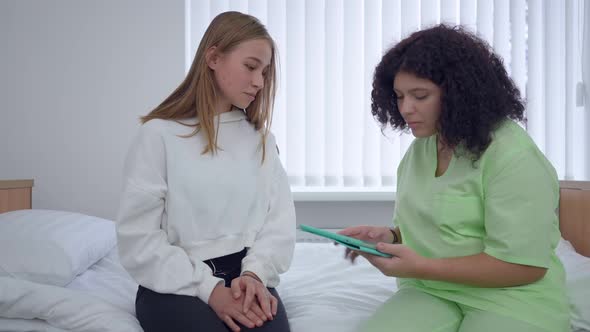 Beautiful Young Woman Sitting on Bed in Hospital Ward As Doctor Checking Online History Endorsing