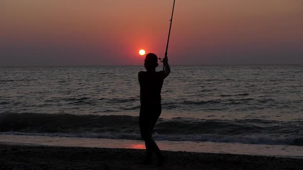 Silhouette of a Child with a Fishing Rod Against the Background of a Sea Sunset