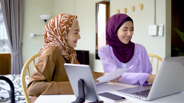 Two asian muslim women working together with using laptop pc tablet and paper graphic chart 
