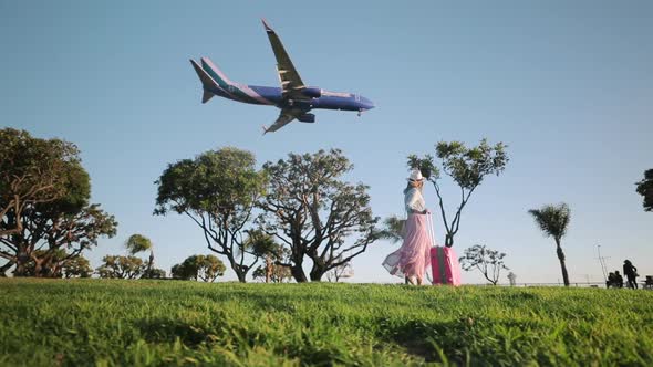 Slow Motion Arriving Airliner at the Airport. Traveler with Suitcase at Sunset