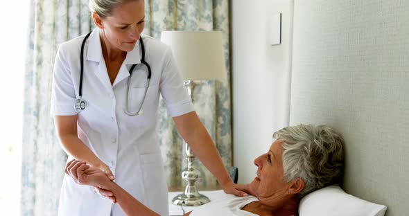 Female doctor checking senior woman pulse during check up in bedroom