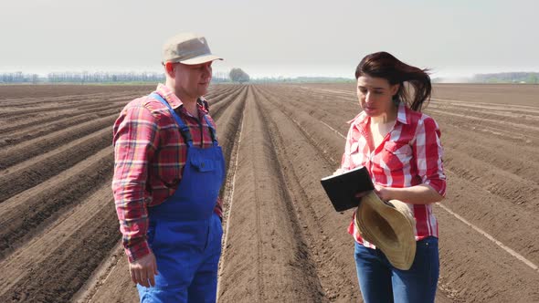 Farmer and Agronomist Stands Between Soil Rows, Furrows on Field, with Digital Tablet, Talking