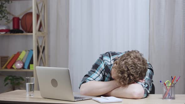 Young Tired Man in Checkered Shirt Sleeps at Table Wakes Up and Types on Laptop Keyboard