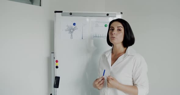 Female Speaker Conducts Lecture at Camera Near Whiteboard in Office