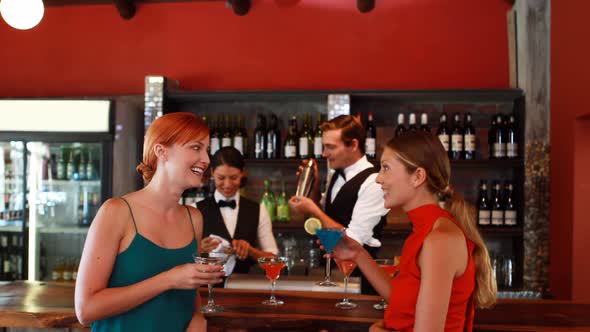 Two women with cocktail drinks talking to each other at counter