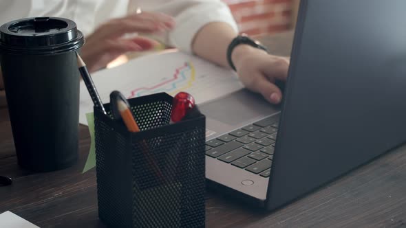 Businesswoman typing hands on laptop, sitting at office table, and takes a sip of coffee