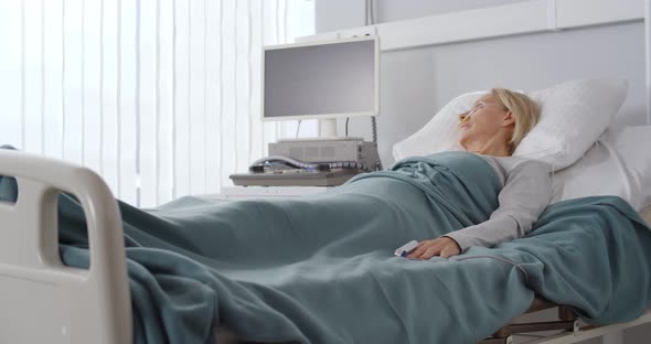 Side View of Sick Senior Woman Lying in Bed in Hospital Ward