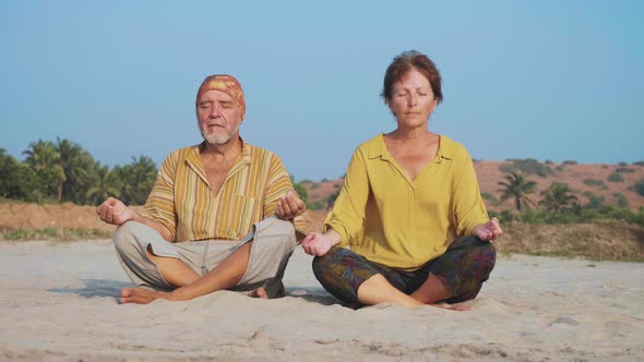 Senior Couple Sits and Meditating Together on Sandy Beach